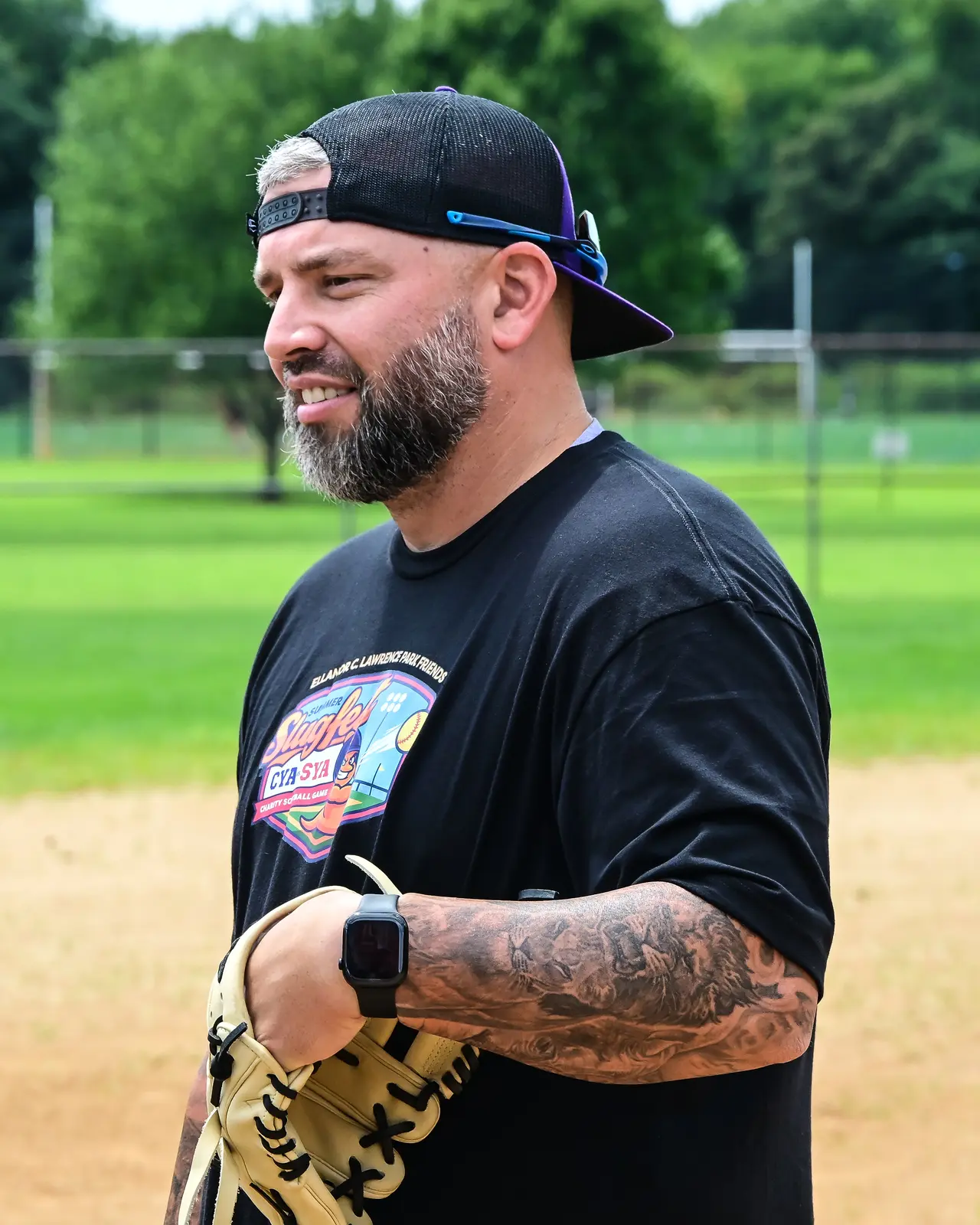 Summer Slugfest softball player in a black event shirt holding a glove beside the field.