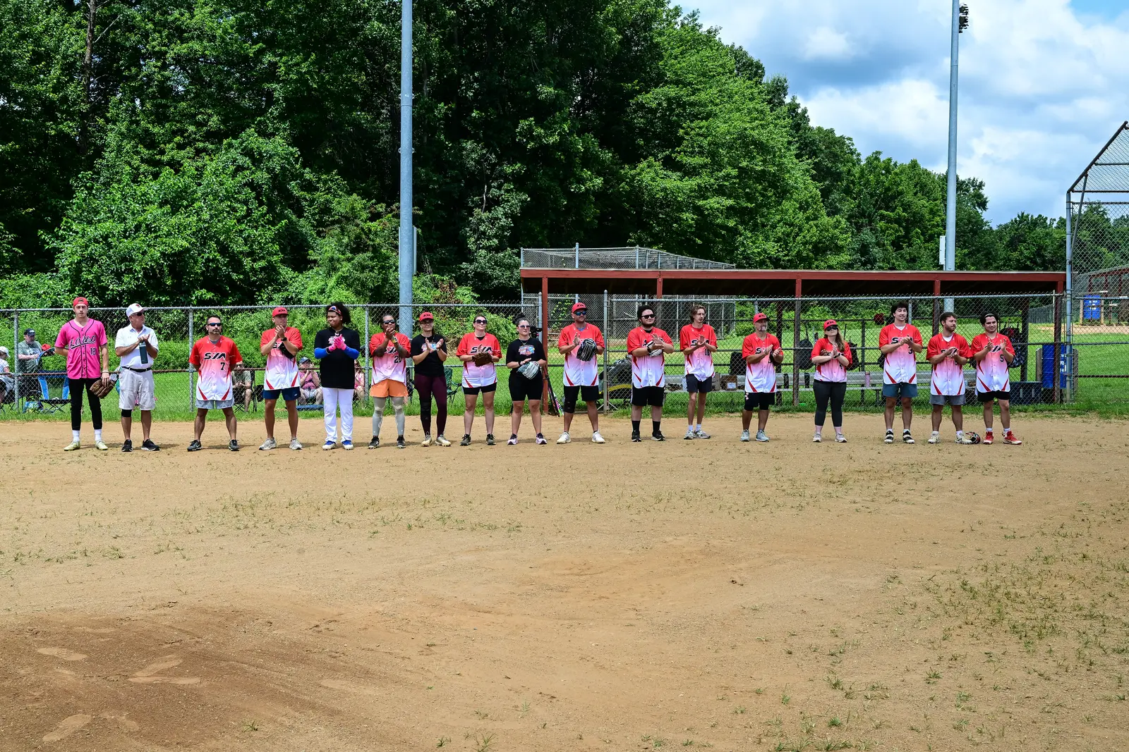 SYA softball players in red jerseys lined up along the baseline before the charity game.