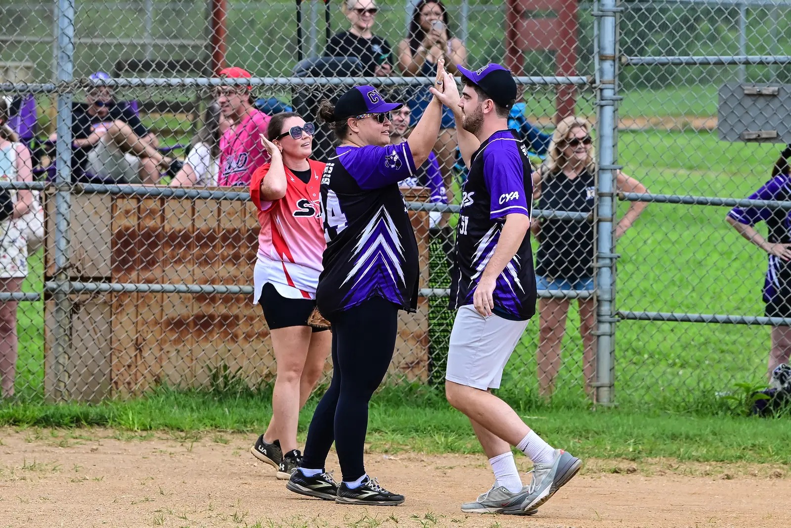 CYA player in purple and SYA player in red exchanging a high-five near home plate.